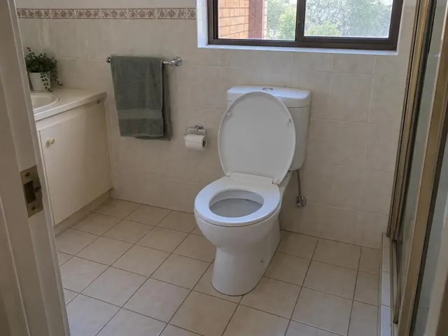 Clean white toilet in a tiled bathroom with a window and towel rail in North Rocks